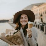 Happy woman with ice cream and flowers by the riverside in a stylish outfit.